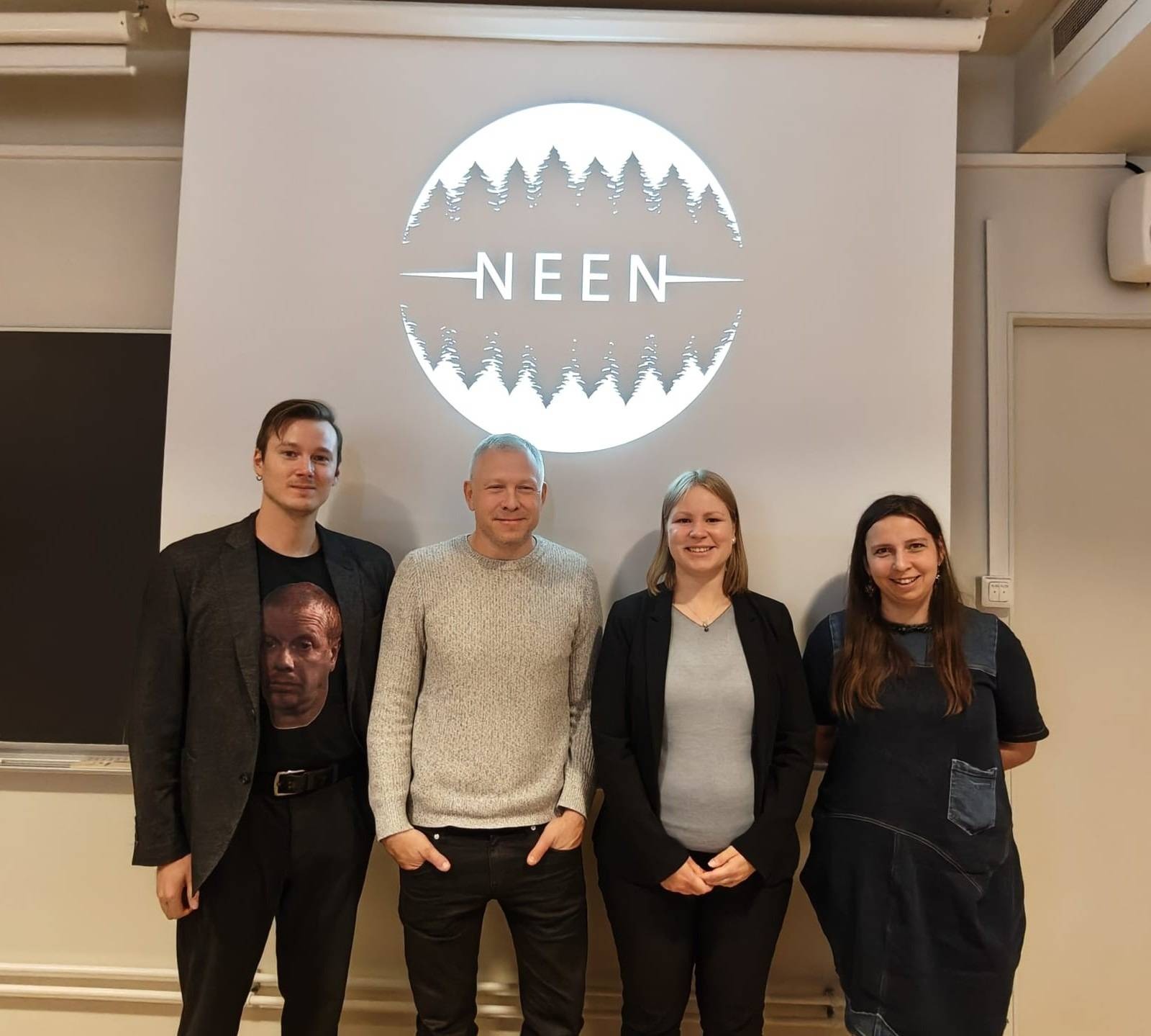 Attēlā redzami četri pētnieki, kuriem fonā ir prezentācijas ekrāns ar Nordic Environmental Ethics Network logo. Pirmā no kreisās puses ir projekta pētniece Anne Sauka.